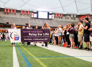 Heather Buchan, a senior advertising major who has been cancer free for four years, stands on the far left of the banner, while Katherine Frega, a junior who has been cancer free for three years, stands on the far right of the banner. At Relay for Life, those who have battled cancer carried a banner around the Carrier Dome. 