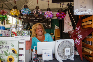 Martee Crowley, owner of Murals and More by Martee, sits at her booth selling her glasswork.