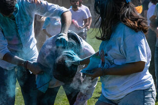 Clouds of blue powder rise as people spread powder on clothes, faces, arms and hair. 